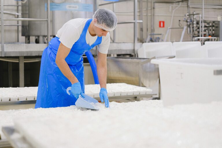 A factory worker in a blue apron processes milk in an industrial dairy plant.